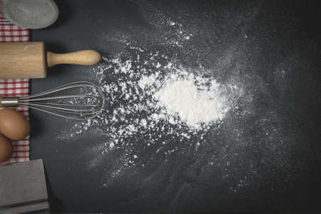 Wooden dough roller and whisk on the black table with flour spread. Bakery homemade concept.の写真素材