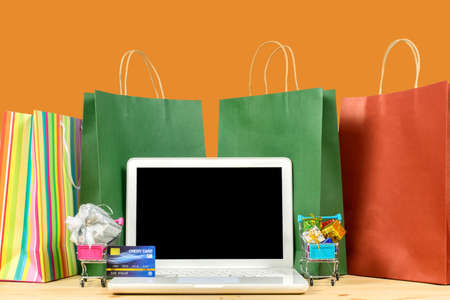 Paper shopping bags, laptop with credit card and trolley carts with full of gives on the wooden table. concept. Concept online sale. saleの写真素材