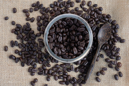 Roasted coffee beans in a glass jar with wooden spoon on sackcloth background. Background of roasted...