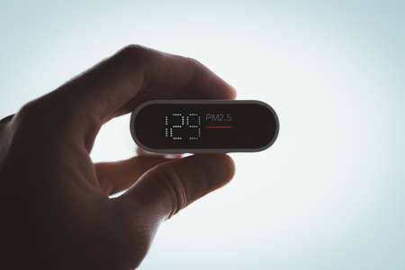 Close Up hand holding air quality monitor to detect level of pollution or small particle (PM2.5) on sky background. image high pollution concept.の写真素材