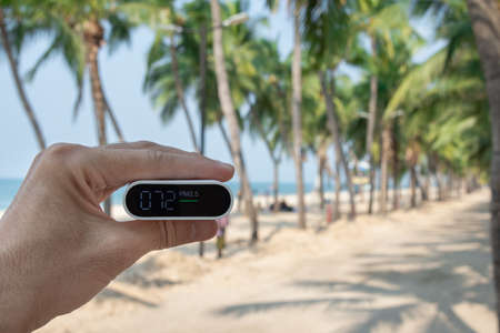 Close Up hand holding air quality monitor to detect level of pollution or small particle (PM2.5) on sea and beach background.の写真素材