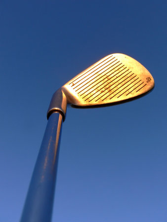 A golf club held up against the blue sky, the evening light makes it glowの写真素材