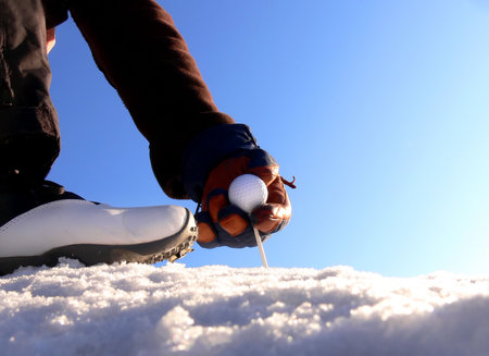 Close-up of a golfer teeing up in the snow a clear cold day の写真素材