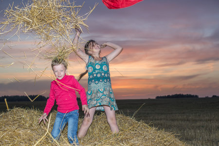 Boy and girl standing on a stack of straw yellow, jump and throw her up against the setting, the...