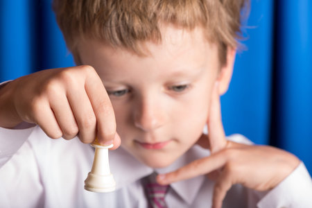 boy in white shirt playing chess on a blue backgroundの写真素材