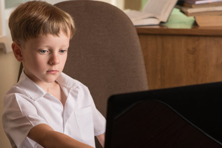 boy with laptop at the table looking at the monitor and presses a key on the keyboard