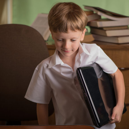 a boy carries a laptop under his arm preparing to workの写真素材