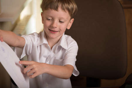 boy sitting at table with laptop and holding a sheet of paperの写真素材