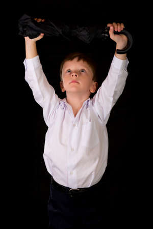 Portrait of a boy on a black background with the white shirt. Blue eyes blond. With umbrella in hand while standing.の写真素材