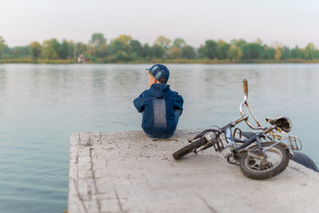 The child is traveling down the river on a bike in the summer. On the pier looking into the...