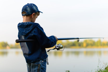 Attentive , focused, serious child is on a summer fishing on the river with a fishing rod in his...