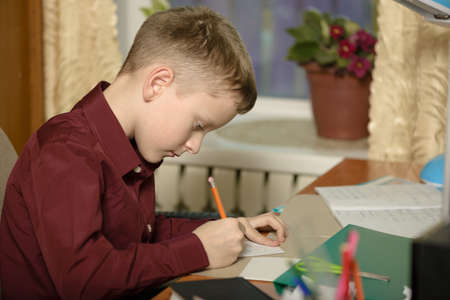The guy at the office uses computer technology.He writes his thoughts on a piece of paper. Sits in an armchair dressed in a burgundy shirt.の写真素材