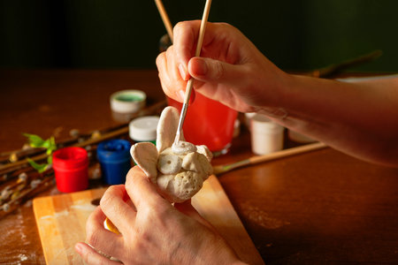 The artist paints religious objects. Easter bunny prepared for coloring is lying on the board....