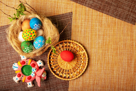 Easter still life. A nest of straw and flax with painted eggs and a rabbit. Wicker basket stands on...