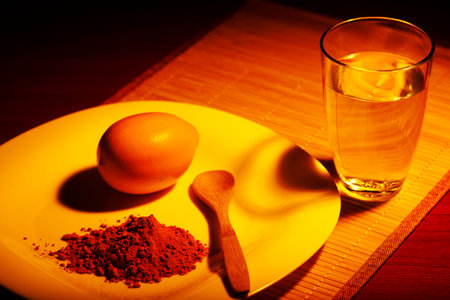 On a napkin from a bamboo there is a cup with a turmeric, a lemon and a glass of water. The ground...