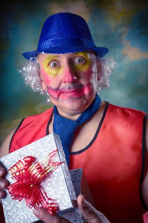 A man in a clown costume. A blue hat on his head, and a tie around his neck, a red vest. Foolish...