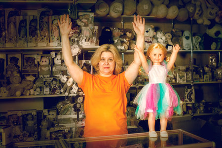 A woman is holding a doll in front of a shelf full of stuffed animals. The doll is wearing a colorful dressの写真素材