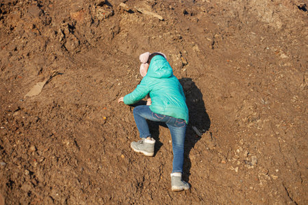 A girl is climbing a mountain. The child is dirty clothes.