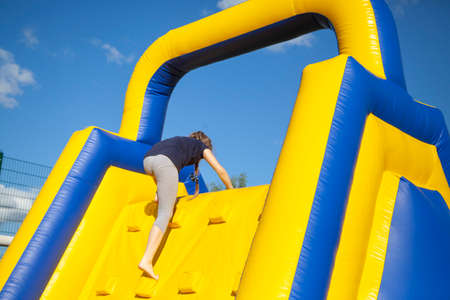 Inflatable obstacle for fun. People climb the hill. Children's area for jumping. Inflatable city. Trampoline center in the open air. The guys climb the wall.の写真素材