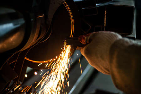 Metal cutting. Grinding steel. Work as a grinder. Sparks from friction. Men's work. Creating a design. The project in the workshop. Iron processing. Hand electric tool.の写真素材