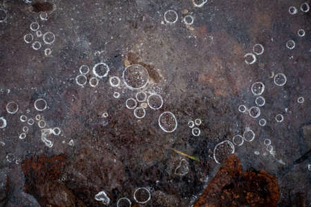 Bubbles of air in frozen water. The texture of the ice in nature. Beautiful natural background of frozen bubbles. Ice crust on the ground. The temperature is below zero. Winter has come. Background for design.の写真素材
