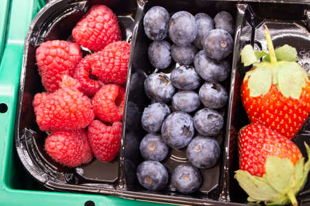 Fresh berries are packed in trays. Vitamin-rich fruits are packaged in boxes. A variety of fruits for sale in a store. Tasty berries.の写真素材