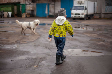 A child on a walk.  The guy in the bright jacket has fun on the street. Funny little boy. Rubber boots on the feet of the child.の写真素材