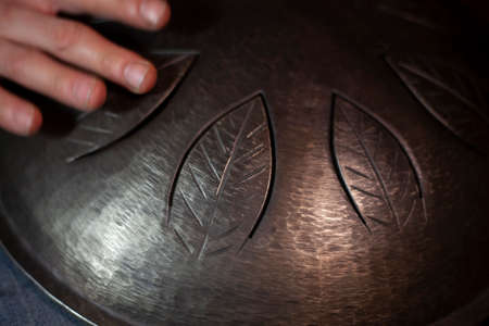 Playing the drum of metal. Meditative music. Hang is a sheet music game on metal plates. Music lesson. Beating the rhythm. Making sound. Musical instrument traveler. Space sound.の写真素材