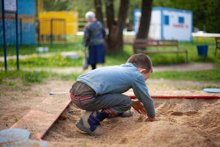 A child picks up sand. A boy plays in the sandbox. Walk with the child on a sunny day in the playground. The development of fine motor skills in a boy. Active lifestyle in children. Fine sand pours from hands.の写真素材