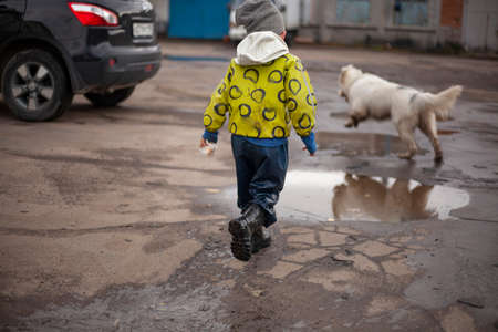 A child on a walk.  The guy in the bright jacket has fun on the street. Funny little boy. Rubber boots on the feet of the child.の写真素材