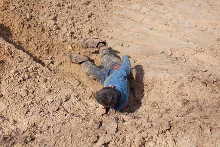 The boy is lying in the sand. The kid is dirty clothes. The boy fell in the sandbox. Naughty child having fun. A child without movement after falling. Rest of the child without the Internet. The usual walk with the children.の写真素材