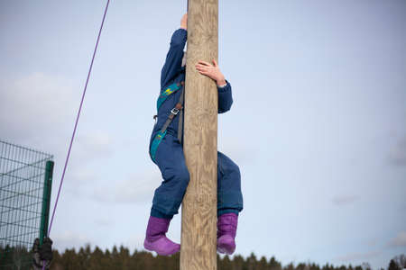 Children's mountain climbing. A girl climbs on a pole. A child with insurance climbs a tall pole. Fun in the park. Physical exercise to develop coordination of movement. A lesson in a physical training camp.の写真素材