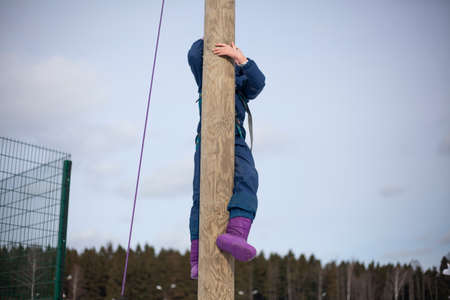 Children's mountain climbing. A girl climbs on a pole. A child with insurance climbs a tall pole. Fun in the park. Physical exercise to develop coordination of movement. A lesson in a physical training camp.の写真素材