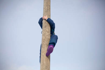 Children's mountain climbing. A girl climbs on a pole. A child with insurance climbs a tall pole. Fun in the park. Physical exercise to develop coordination of movement. A lesson in a physical training camp.の写真素材