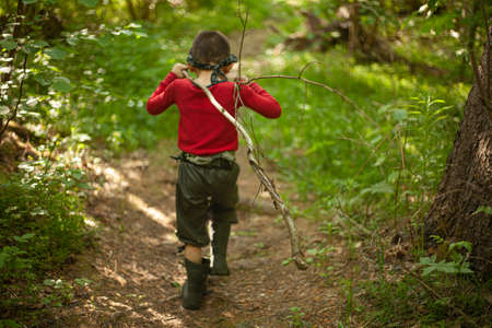 The boy walks through the woods alone. A child in a red sweater is among the plants. A five-year-old boy spends time in the forest. Camping. The child got lost in the forest. Lost children.の写真素材
