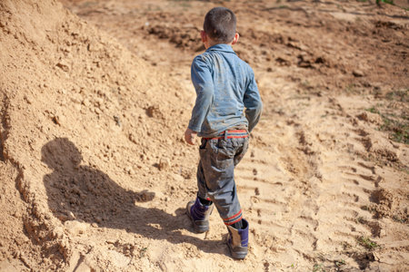 A child plays in the sand. The boy is dirty clothes in a mountainA boy plays in the sandbox. of...