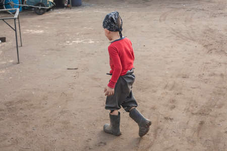 A boy plays with a cart on the street. A child in his fathers garage found amusement. Active child uses force. Energetic boy on a sunny day in the dust pushes a wheelbarrow. Children without gadgets.の写真素材