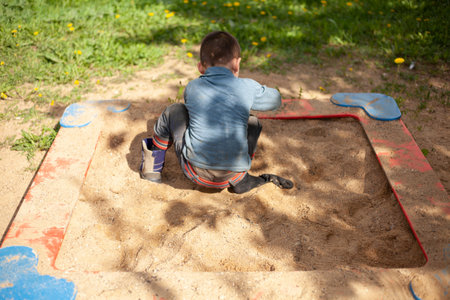 A child is gaining sand in a shoe. Playing son at the playground. Children's rest in the summer in the yard. Activities for children. Soiled clothes on the baby. Walk in the fresh air. The development of hand motility.の写真素材