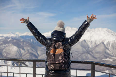 The girl on top of the mountain raised her hands up. Reaching the goal. Success in human gestures. The joy of victory. Travel to the snowy mountains. Mountain ski resort.の写真素材