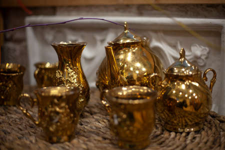 A kettle and other dishes of gold color. Cafe subject shooting. Drinks are set on the table. Service for lunch. Tea party preparation. Cozy grandmother's dishes for the home. Vintage household utensils. Gold service.の写真素材