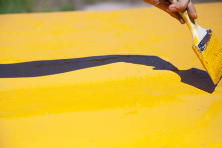 Yellow paint is applied to the surface. The painter does the work. Application of a coat of paint. Sunny day. Bright yellow color.の写真素材