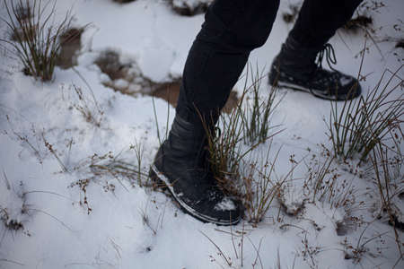 Army shoes on a girl. The legs of a teenager. Quick step in the snow. Black clothes in a teenager. Walk in the cold. An unknown person left traces. Escape from home. Leap in place.の写真素材