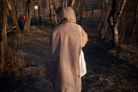 The girl walks in the evening in a warm jacket. Woman with a hood on her head. Unknown person in the park. Designer clothes of the original cut on the model. Warm coat for walking in cold weather.の写真素材