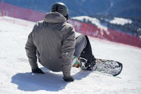 A snowboarder rides on a slope. Rest on the top of the mountain. Mountain ski resort. The guy is rolling down the mountain. Hobbies for young people. Holidays in the winter on a slope for snowboarding.の写真素材