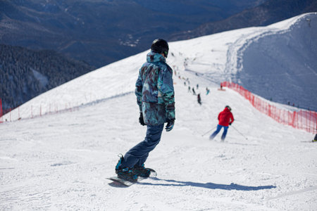 A snowboarder rides on a slope. Rest on the top of the mountain. Mountain ski resort. The guy is...