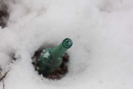 Bottle in the snow. A blue glass container is immersed in a layer of frozen water. Simple background discarded beer bottle.の写真素材