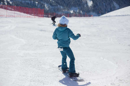 A snowboarder rides on a slope. Rest on the top of the mountain. Mountain ski resort. The guy is rolling down the mountain. Hobbies for young people. Holidays in the winter on a slope for snowboarding.の写真素材