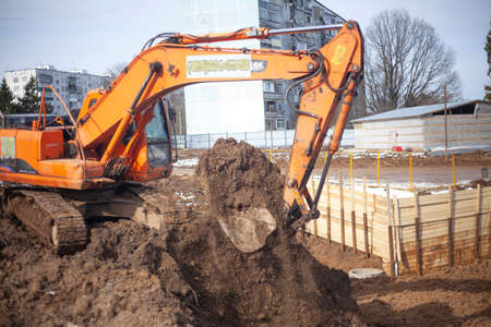 A machine at a construction site digs the ground. An escalator is preparing a construction site. Building a house. The work of heavy equipment. Preparation of the foundation of the house. Construction of a residential complex.の写真素材