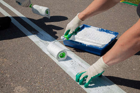 White line on the pavement. Drawing markup for a bike path. Beautification of the park. The work of a house painter on the street. Paint roller with white paint.の写真素材