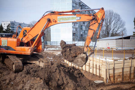 A machine at a construction site digs the ground. An escalator is preparing a construction site. Building a house. The work of heavy equipment. Preparation of the foundation of the house. Construction of a residential complex.の写真素材